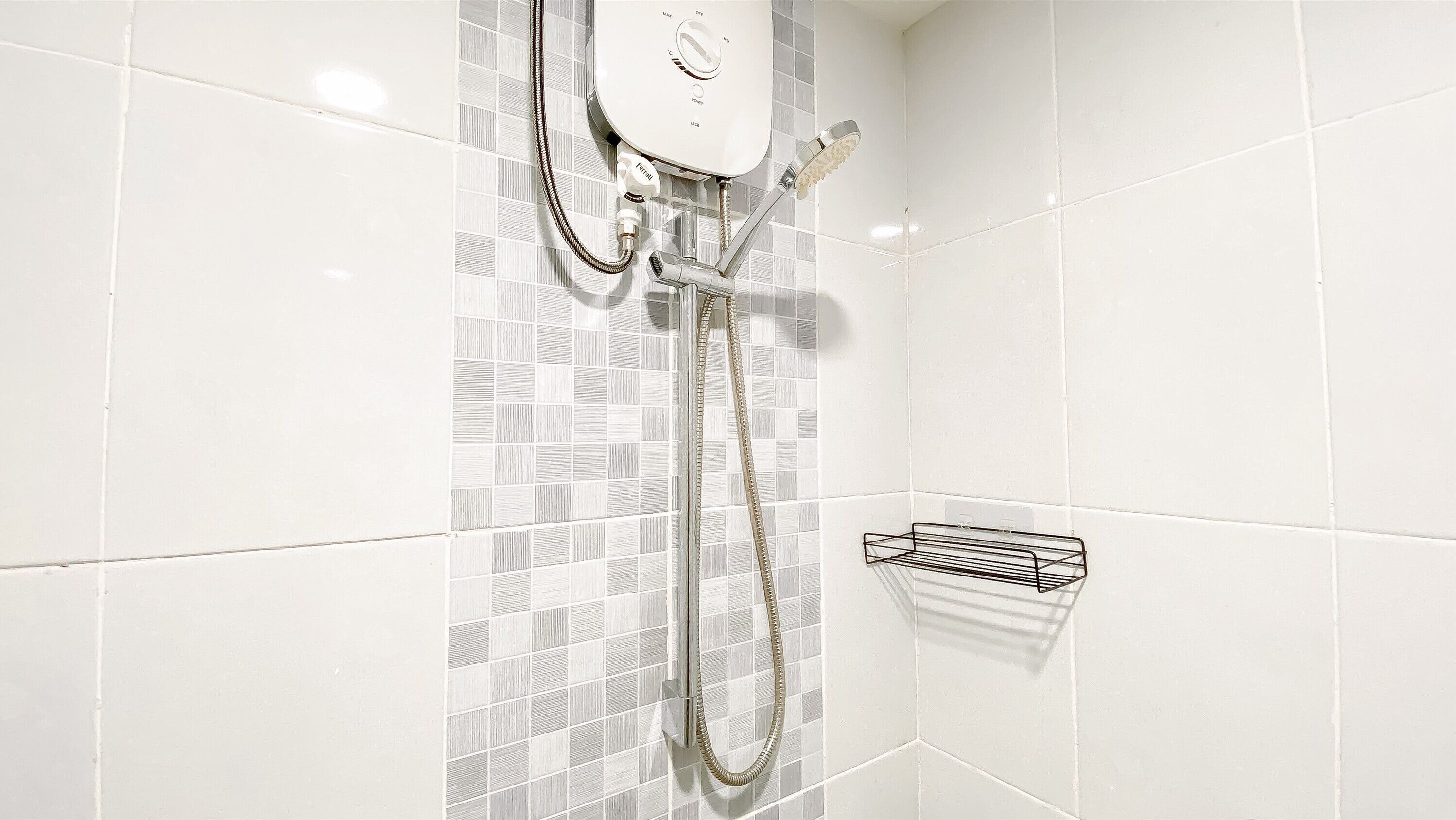 Une douche équipée d’un panneau de commande et d’un pommeau de douche à main, fixée sur un mur carrelé orné de motifs.