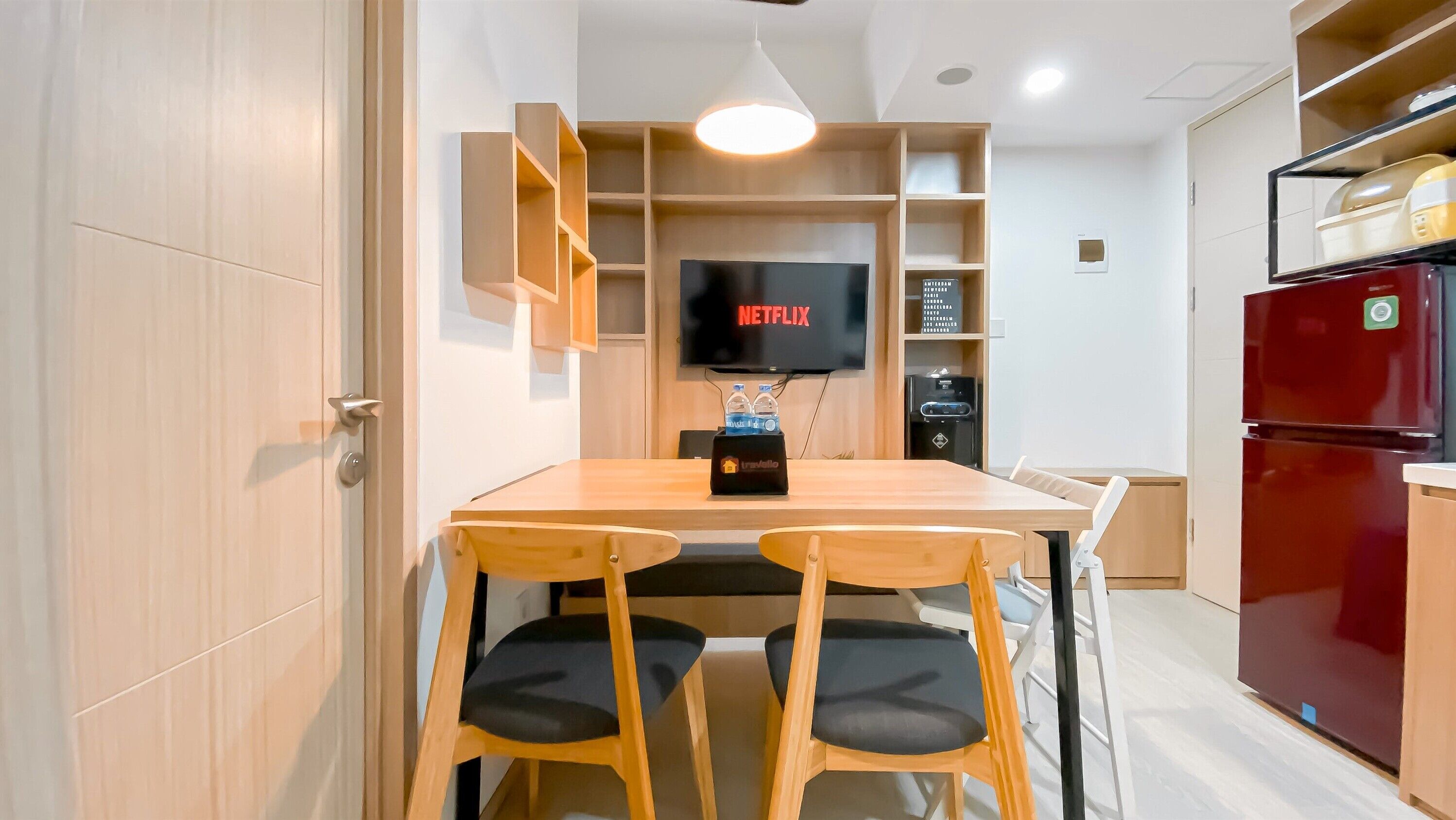 Uma cozinha compacta com mesa de jantar, cadeiras, uma TV instalada acima da mesa e uma geladeira.