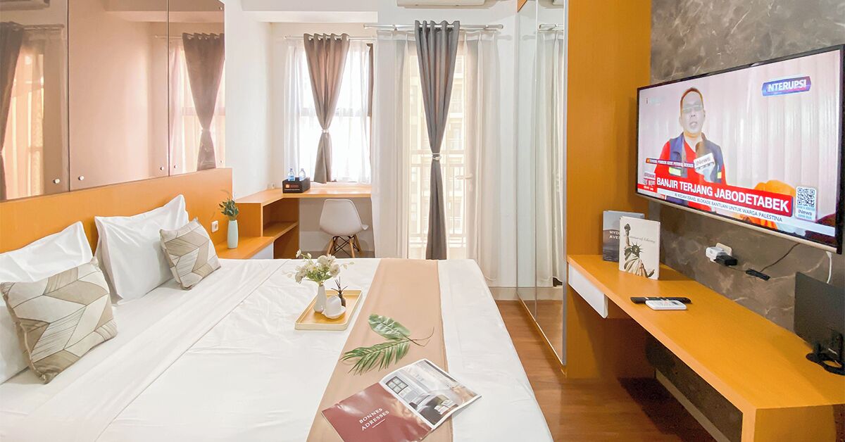 A hotel room with a large bed, a desk, a TV, and a window with curtains.