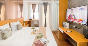 A hotel room with a large bed, a desk, a TV, and a window with curtains. - Best Deal And Minimalist Studio Apartment Transpark Cibubur (Depok)