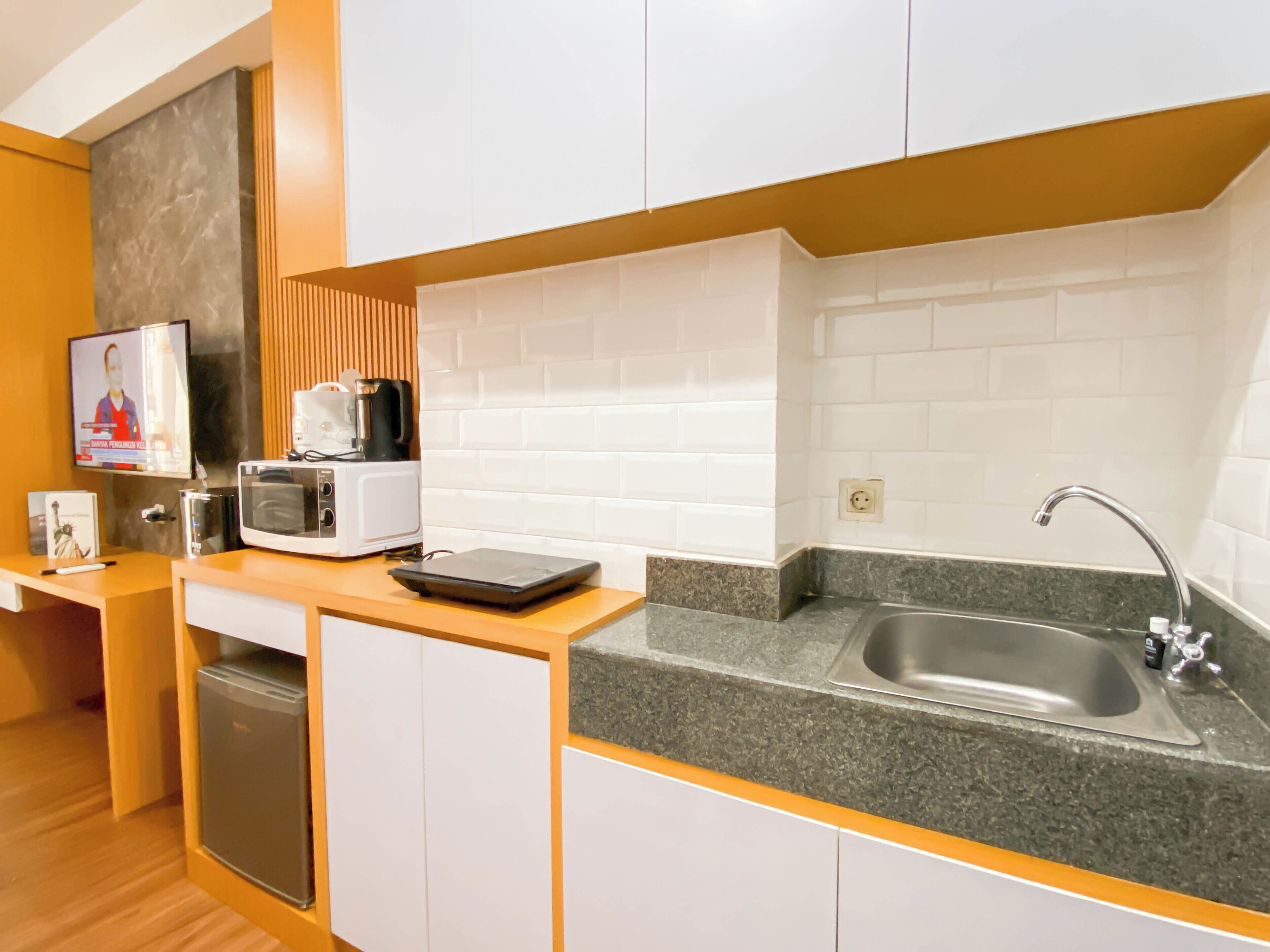 A compact kitchen with white cabinets, a granite countertop, a sink, a microwave, a toaster, and a coffee maker.