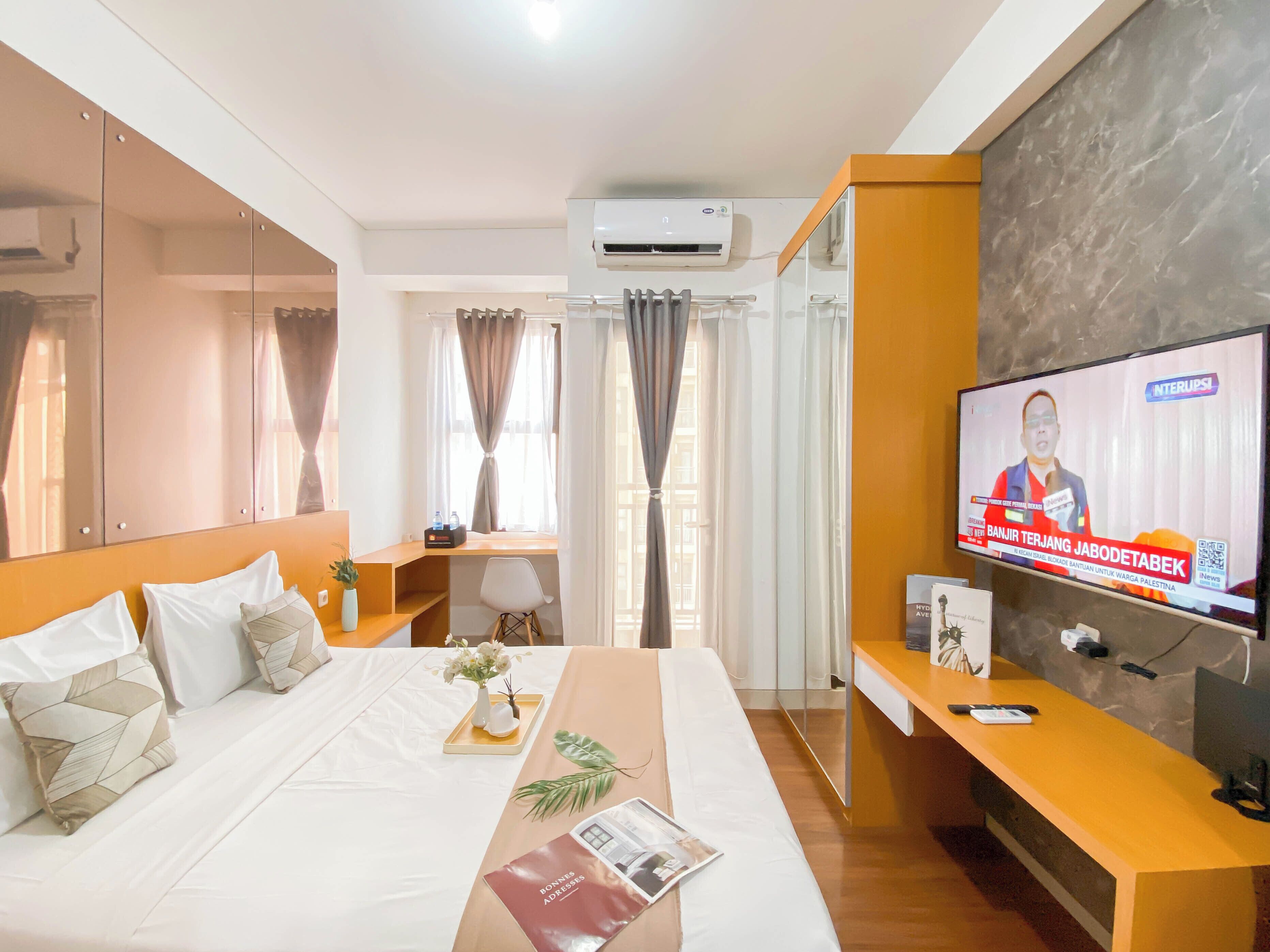Habitación de hotel con cama, escritorio, televisor y ventana con cortinas.