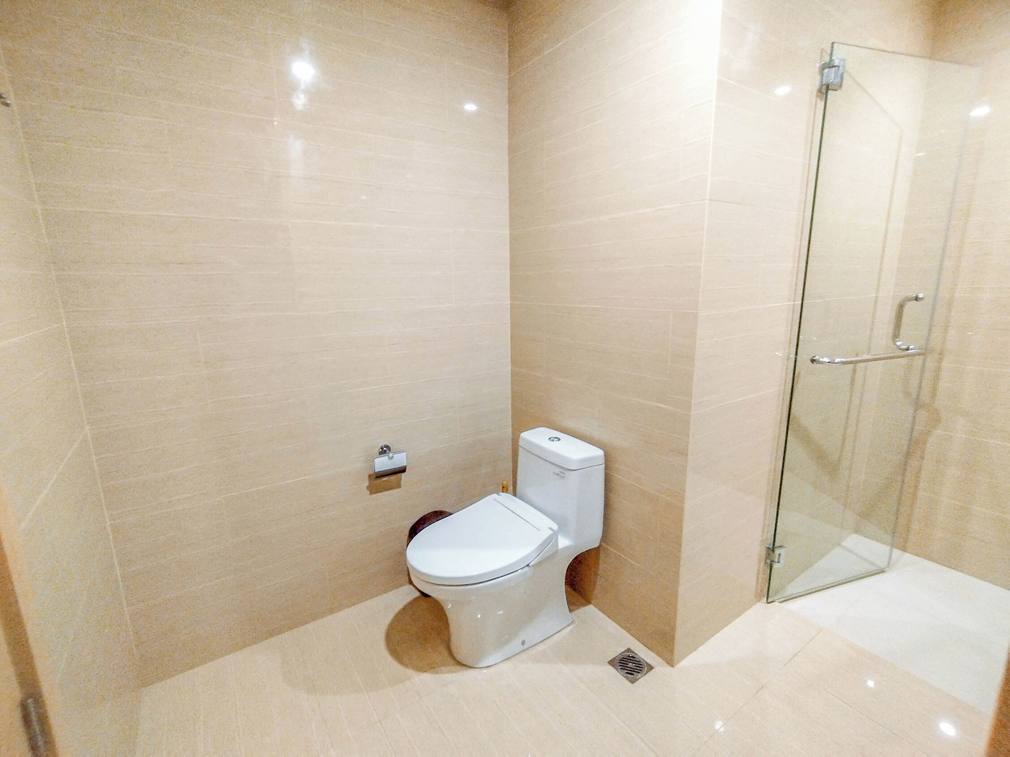A modern bathroom with a toilet, a glass shower enclosure, and beige tiled walls.