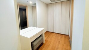 A small, well-lit room with a wooden floor, a white vanity with a mirror, and a wardrobe with vertical sliding doors. - 2Br Luxurious And Spacious Apartment At One East Penthouse Residence (Surabaya)