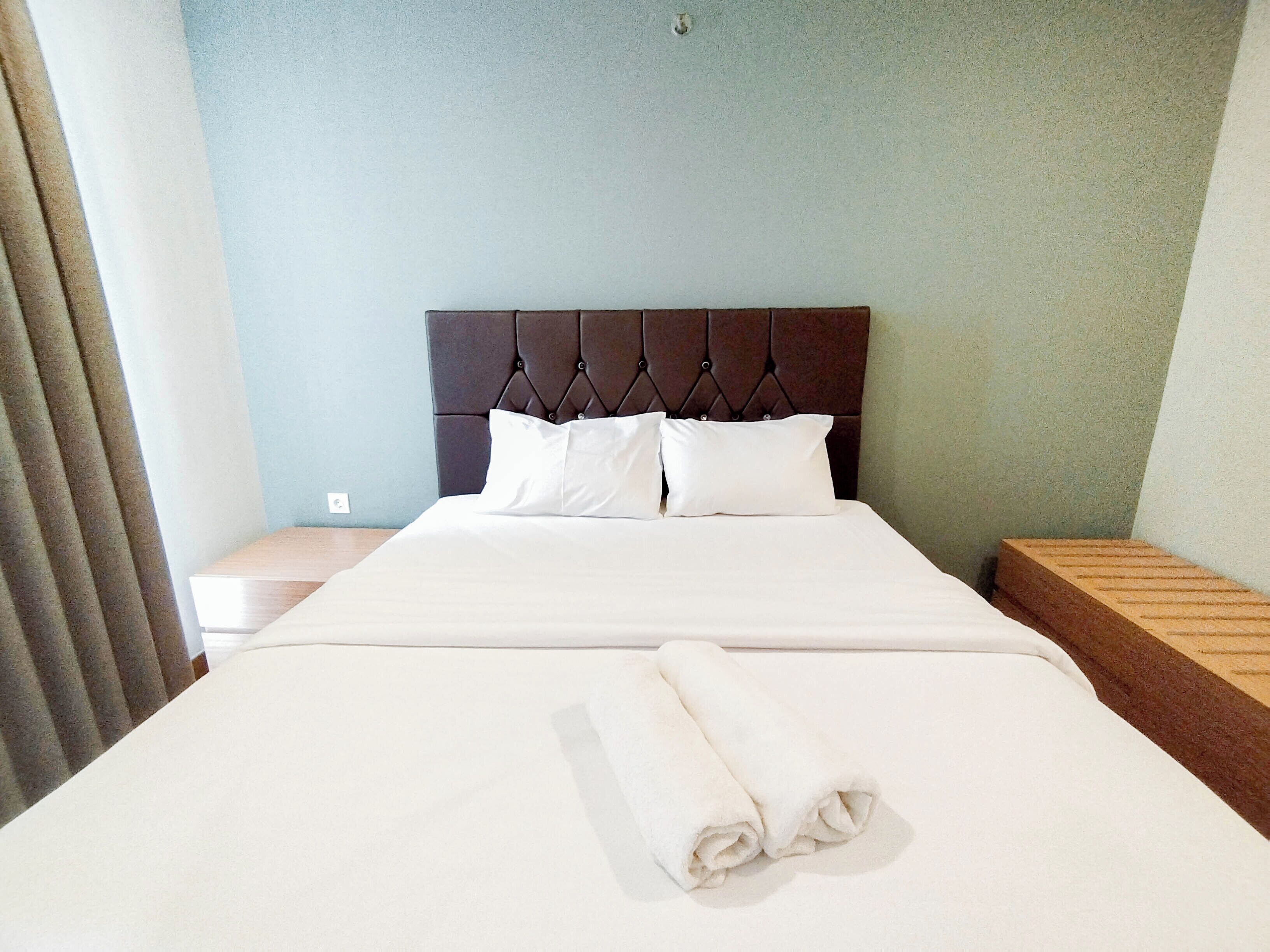 A neatly made bed with white linens and pillows, a wooden headboard, and a wooden nightstand with a lamp.