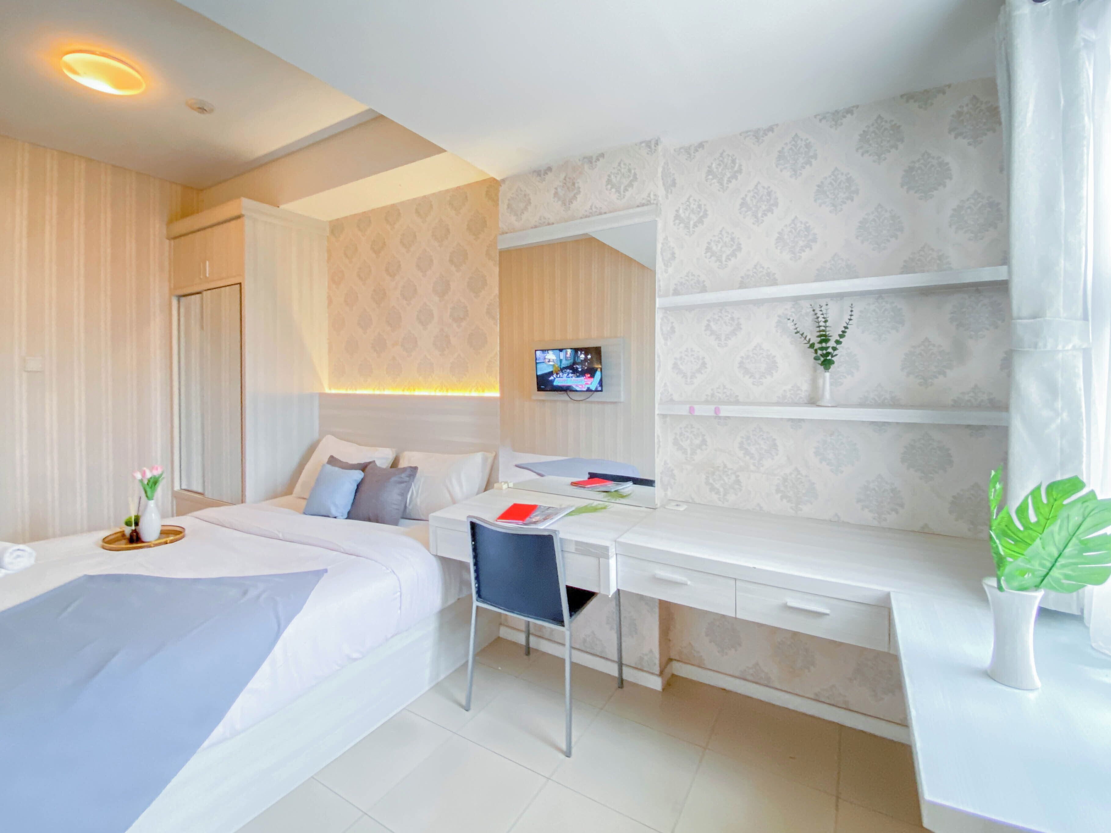 A hotel room with two beds, a desk, a chair, a TV, and a plant.