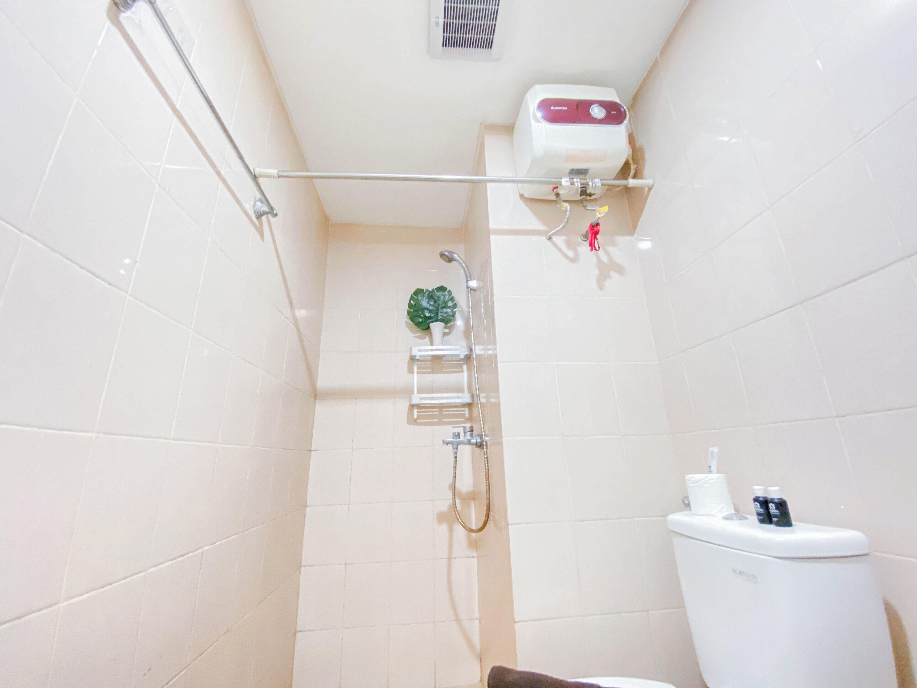 A small bathroom with a toilet, a shower, and a shelf with toiletries.