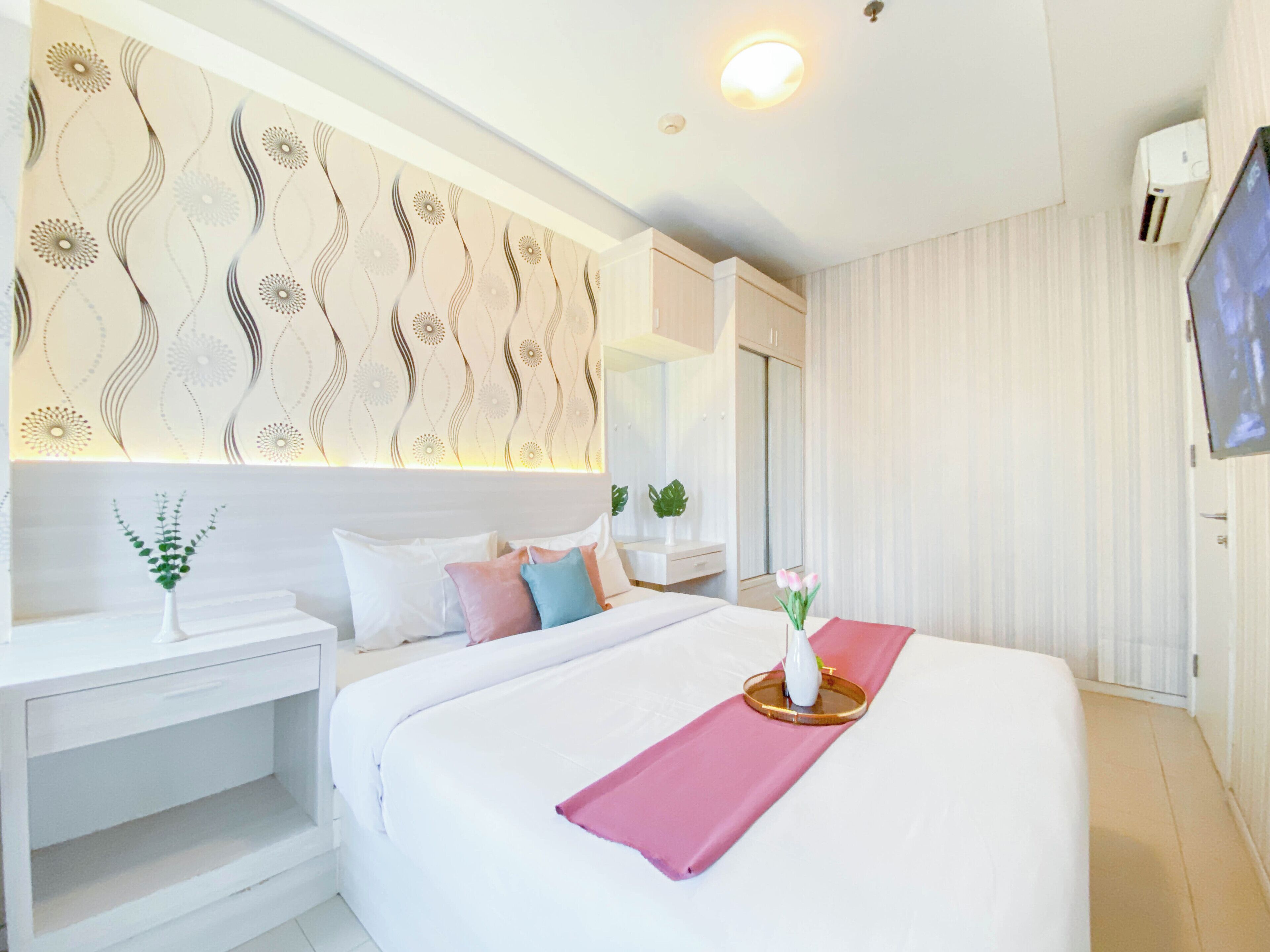 Ein modernes Hotelzimmer mit einem großen Bett, einem Nachttisch, einem Spiegel, einem an der Wand montierten Fernseher und einer Wanddekoration.