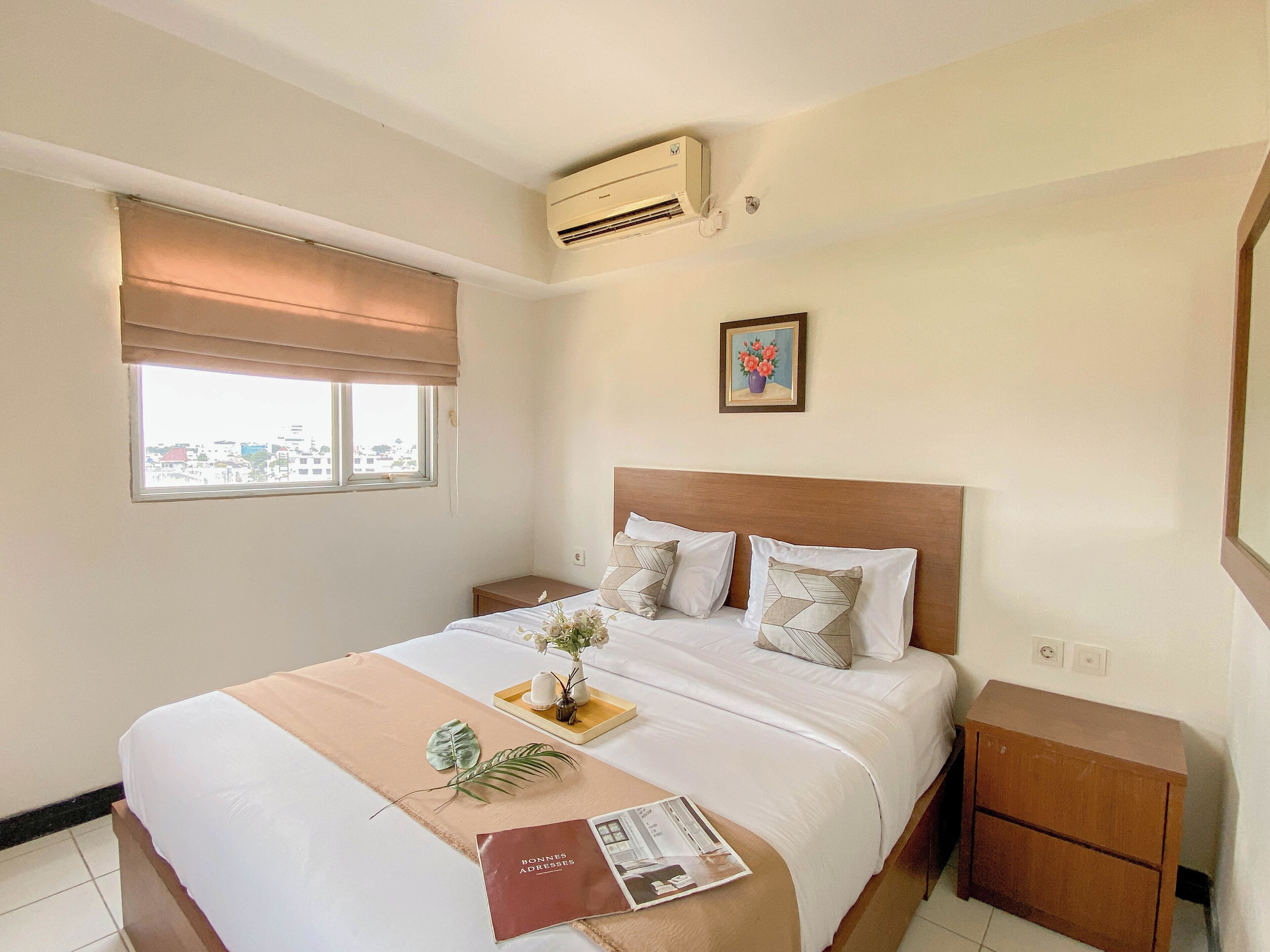 Ein Hotelzimmer mit Bett, Nachttisch, Fenster mit Blick, Klimaanlage und einem gerahmten Bild an der Wand.
