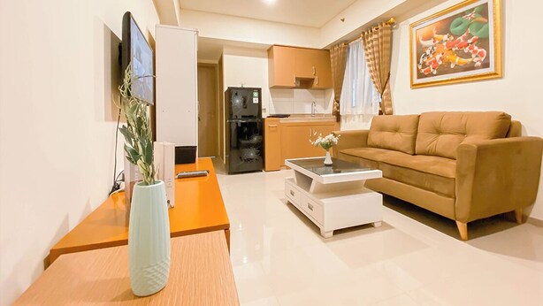 A living room with a sofa, a coffee table, a TV, and a kitchen in the background.