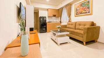 A living room with a sofa, a coffee table, a TV, and a kitchen in the background.
