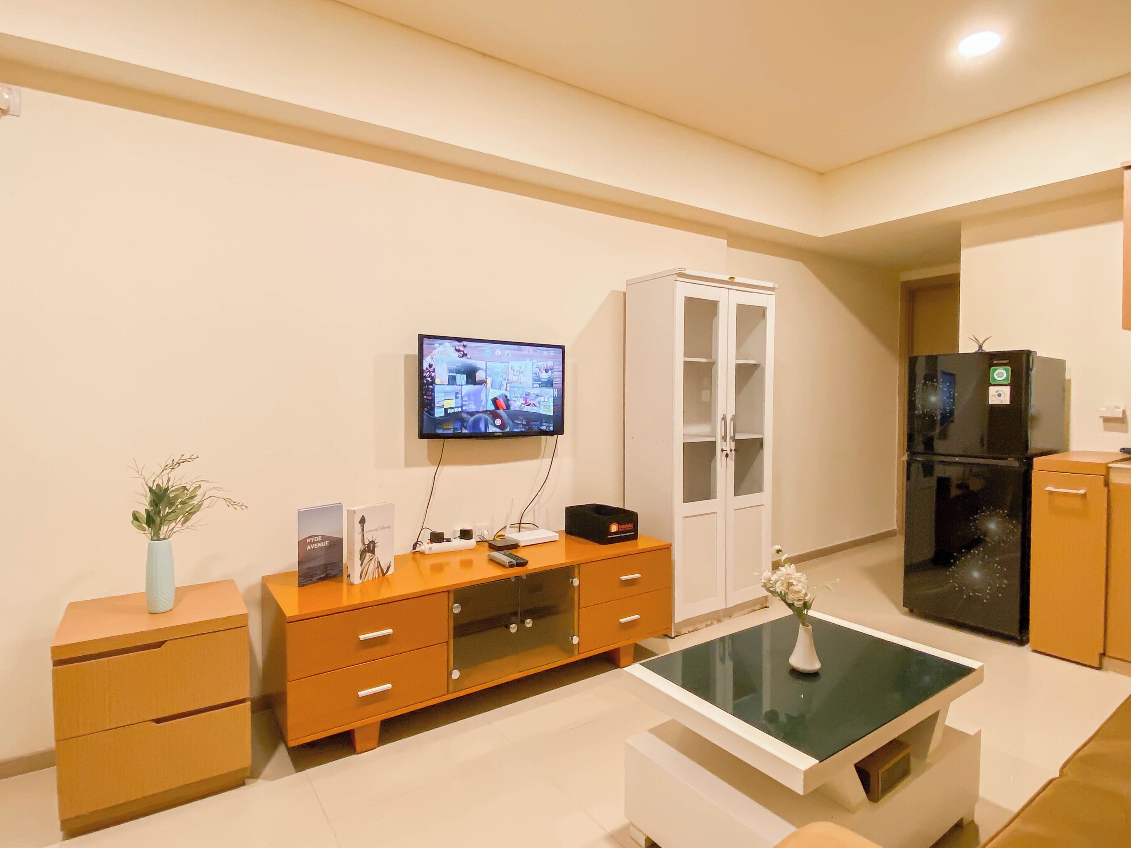 A modern kitchen with a built-in oven, a refrigerator, a TV mounted on the wall, and a wooden cabinet with drawers.