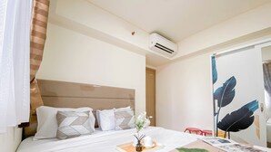A hotel room with a bed, a bedside table with a tray, a mirror, and an air conditioning unit.