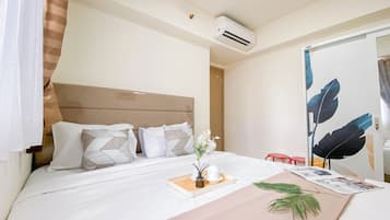 A hotel room with a bed, a bedside table with a tray, a mirror, and an air conditioning unit.