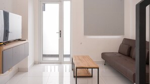 A modern living room with a flat-screen TV, a wooden coffee table, a brown sofa, and a sliding glass door leading to an outdoor area.