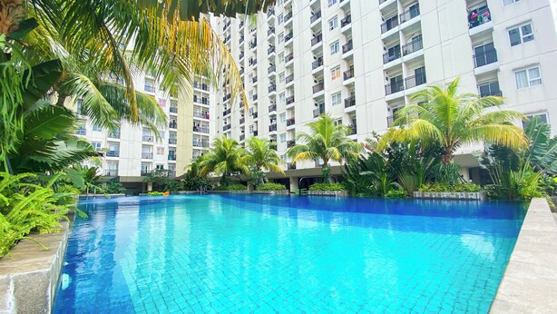 A swimming pool surrounded by lush greenery and a high-rise building with balconies. - Well Furnished Studio Apartment At Cinere Resort (Depok)