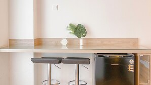 A kitchen with a glass countertop, two black bar stools, a small potted plant, and a black refrigerator. - Well Furnished Studio Apartment At Cinere Resort (Depok)