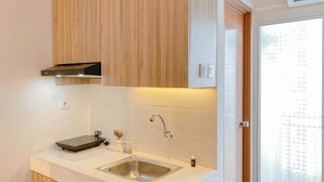 A modern kitchen with a stainless steel sink, wooden cabinets, and a white countertop. - Well Furnished Studio Apartment At Cinere Resort (Depok)
