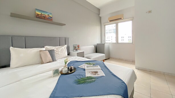 A modern hotel room with a large bed, a small sofa, a window with a city view, and a painting on the wall. - Good Deal And Homey Studio Apartment At Margonda Residence 1 (Depok)