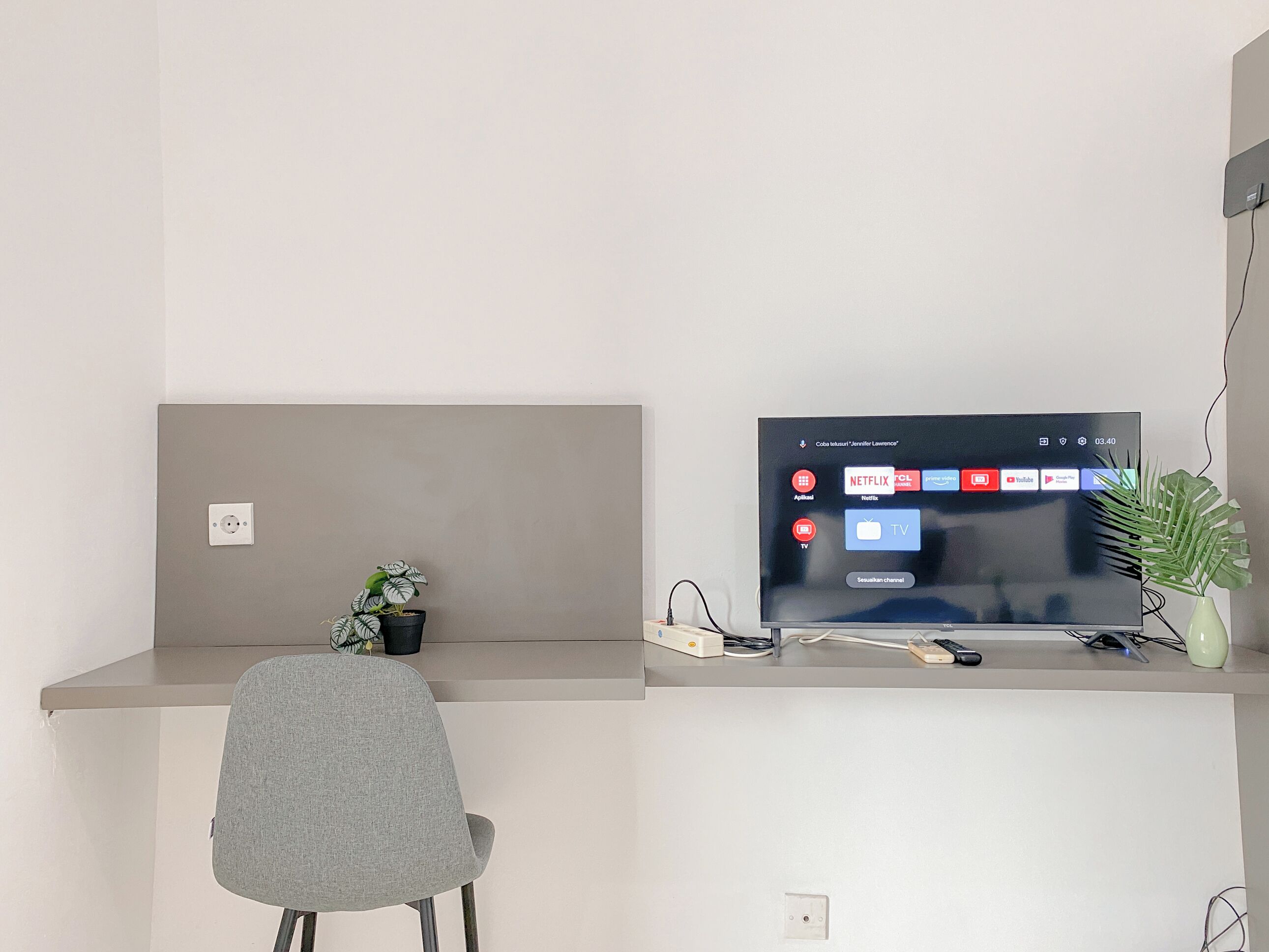 Un espacio de oficina moderno con un escritorio, una silla, un televisor y una pequeña planta en maceta.