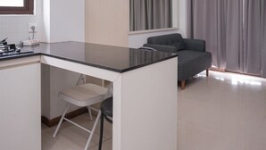 A compact kitchen with a dining area, a window with curtains, and a grey sofa.