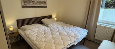 Een enkel bed met een gewatteerde deken, een bedlampje, een klein tafeltje en een ingelijste foto aan de muur.