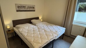 A single bed with a quilted duvet, a bedside lamp, a small table, and a framed picture on the wall. - Apartment for 4 Guest Near Harz Mountains (Clausthal-Zellerfeld)