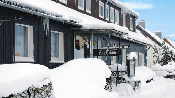 A building with a dark facade and multiple windows, covered in snow and icicles, indicating a cold climate.