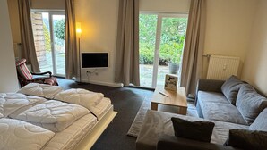 A hotel room with a bed, a sofa, a television, and a view of greenery outside.