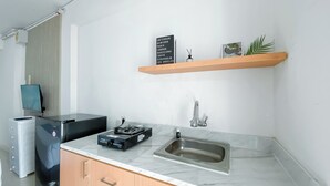 A modern kitchen with a marble countertop, a built-in sink, a Rinnai water heater, and a mounted flat-screen TV. - Brand New Studio At Bassura City Apartment Near Mall (Jakarta)