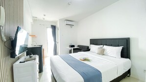 A modern hotel room with a large bed, a desk with a computer, a flat-screen TV, and an air conditioning unit. - Brand New Studio At Bassura City Apartment Near Mall (Jakarta)