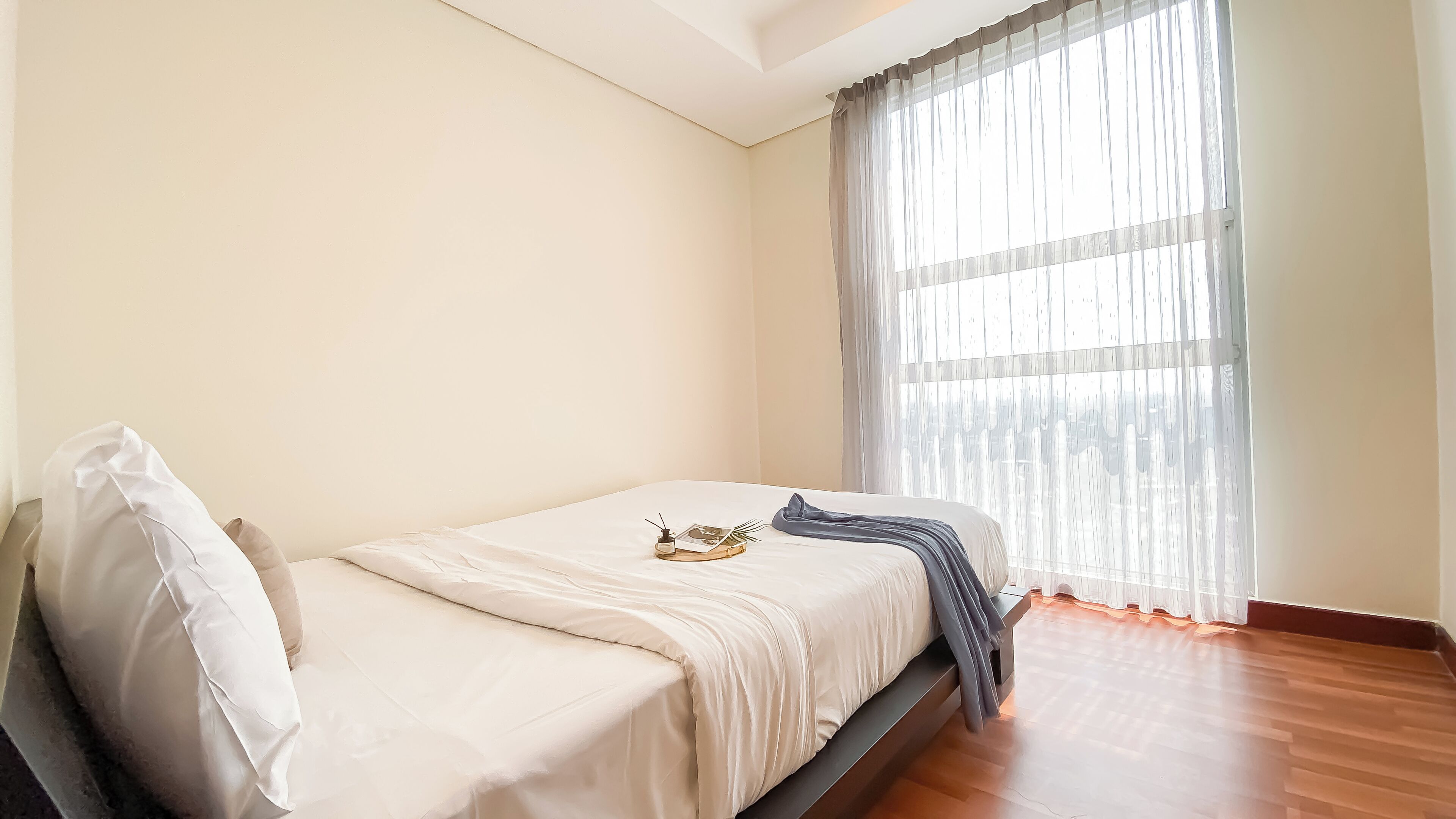 Une chambre à coucher avec un lit, une fenêtre ornée de rideaux légers et un plancher en bois.