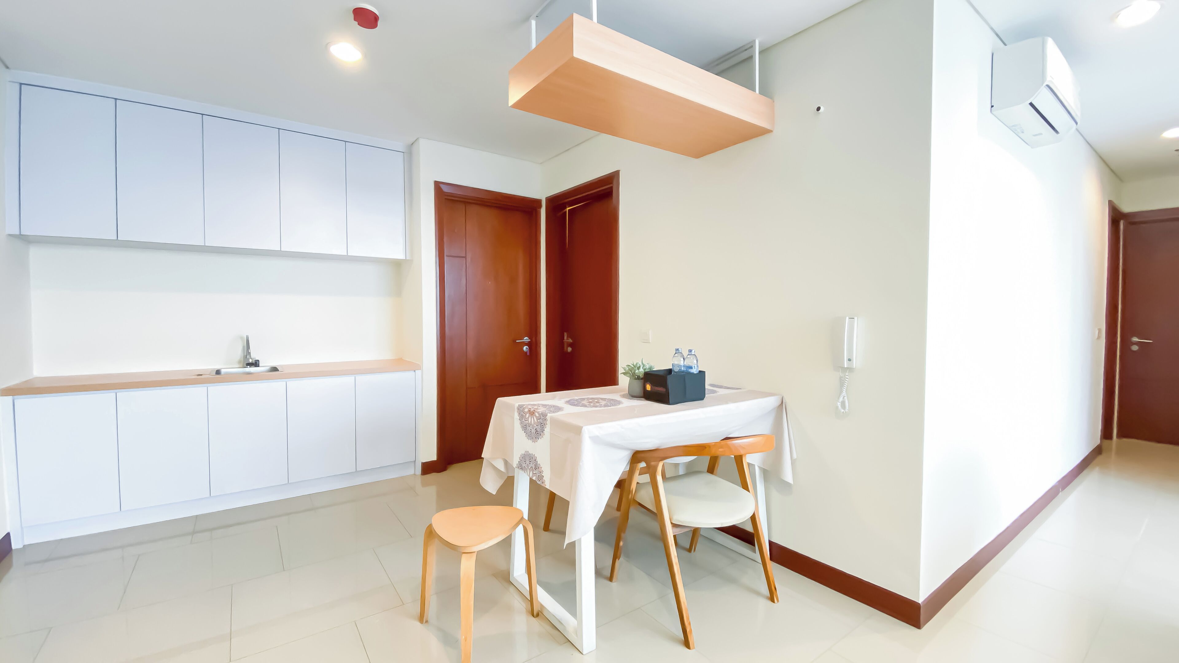 A modern kitchen with white cabinets, a wooden countertop, and a built-in oven. There is a dining area with a table, chairs, and a small stool.