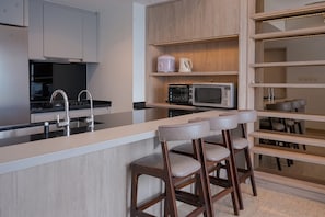 A modern kitchen with a central island, bar stools, a microwave, and a coffee maker. - Spacious And Elegant 3Br At Branz Bsd City Apartment (Pagedangan)