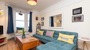 Un salon chaleureux avec un canapé de couleur turquoise, une table basse en bois et une suspension rouge.