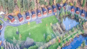 An aerial view of a residential area with multiple houses arranged in a row, a central grassy field, and a pond. - Astbury Falls Escape – A Tranquil Stay in Nature - Pass the Keys (Bridgnorth)