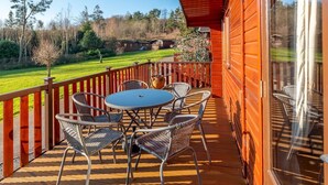 A wooden deck with a table and chairs, overlooking a green landscape. - Astbury Falls Escape – A Tranquil Stay in Nature - Pass the Keys (Bridgnorth)