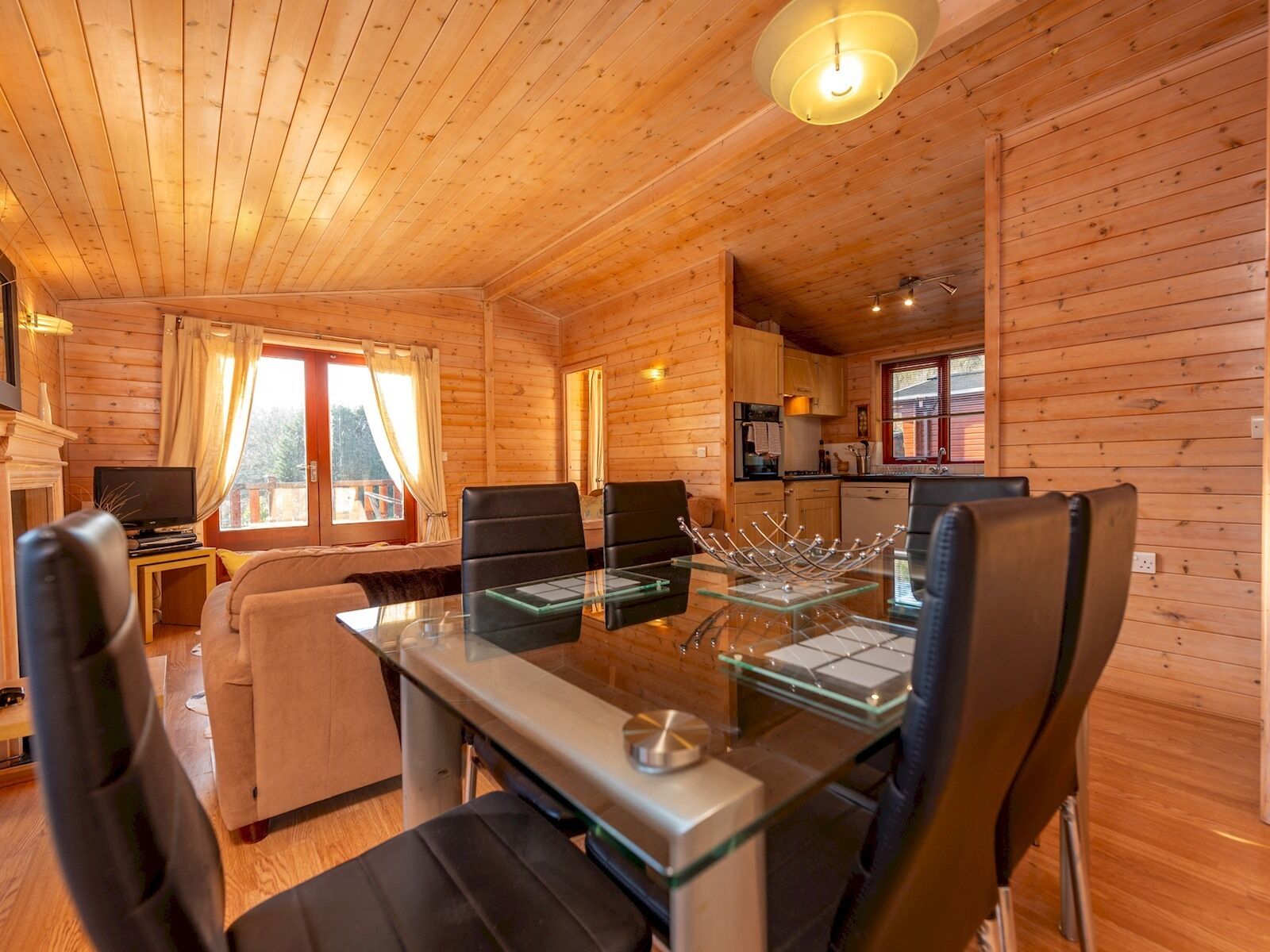 A wooden cabin interior with a dining area, kitchen, and living room.