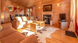 A cozy log cabin interior with a sofa, a fireplace, and a television. - Astbury Falls Escape – A Tranquil Stay in Nature - Pass the Keys (Bridgnorth)