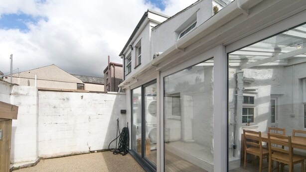 A modern patio area with a glass door leading to a dining space, a white brick wall, and a wooden table with chairs.
