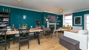 A living room with teal walls, a fireplace, a dining area with a wooden table and chairs, and a sofa.