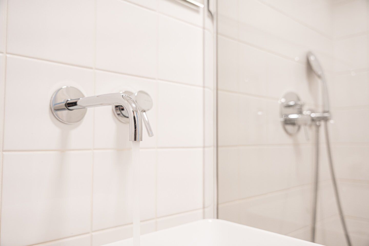 Een badkamer met een witte betegelde muur, een douche met een handdouche en een kraan met hendel.