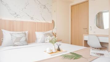 A modern hotel room with a marble headboard, a wooden door, a white desk, and a bed with a tray of toiletries.