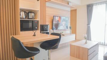 A modern kitchen with a microwave, coffee maker, and a TV on the wall. There are two black bar stools and a wooden table.