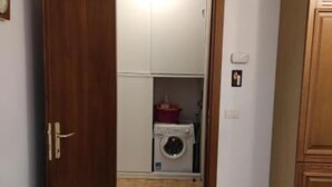 A narrow hallway leading to a laundry room with a washing machine and a red basket. - Two-room apartment Padua strategic area bookable minimum 7 nights max 20 nights. (Padova)