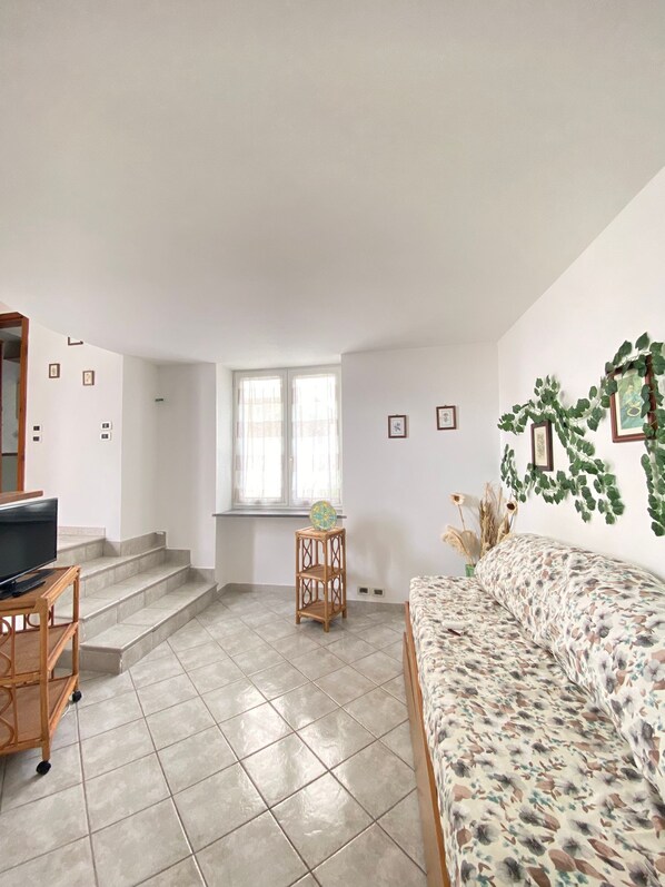Una sala de estar con un sofá, un televisor sobre un mueble bajo, una escalera y un ventanal.