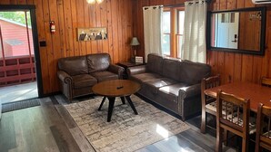 Ein gemütliches Blockhaus-Interieur mit Holzwänden, einem Ledersofa, einem Holzesstisch und einem Deckenventilator.