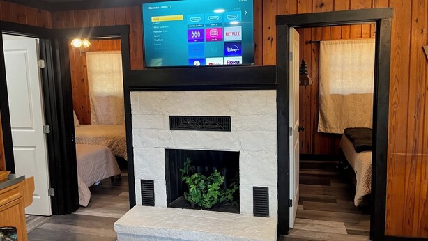 Ein Wohnzimmer mit Kamin, Holzwänden und einem darüber montierten Fernseher, der eine Streaming-Oberfläche anzeigt.