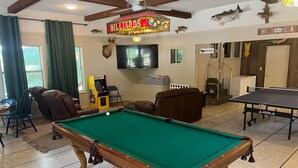 Una mesa de billar en una sala con un letrero de billares, un televisor y un letrero de sala de juegos.