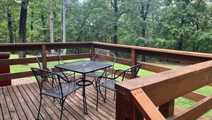 A wooden deck with a metal table and chairs, surrounded by trees. - Castaway Cabin at Fish & Fiddle Family Resort & Extended Stay (Mountain Home)